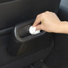 A hand is pressing a white wipe into the opening of a black portable car trash bin.