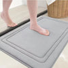 A gray plush memory foam bathroom mat is placed on a tiled floor, showing its texture and non-slip design.