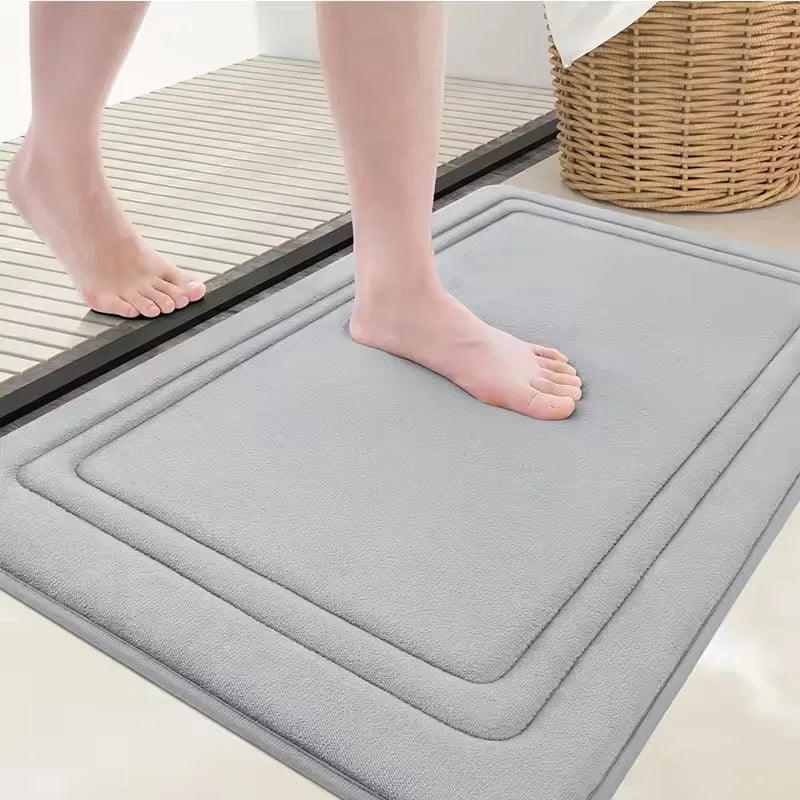 A gray plush memory foam bathroom mat is placed on a tiled floor, showing its texture and non-slip design.