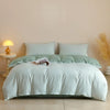 A white quilted duvet cover set with matching pillowcases on a bed, next to a bedside lamp.
