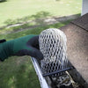 A hand wearing a green glove is installing an aluminum gutter leaf guard mesh onto a roof gutter.