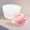 A pink rose-shaped candle is lit in front of a large white silicone mold for crafts.