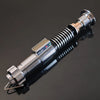 A metallic lightsaber hilt with a Bluetooth motion sensor and blade tip, displayed on a dark reflective surface.