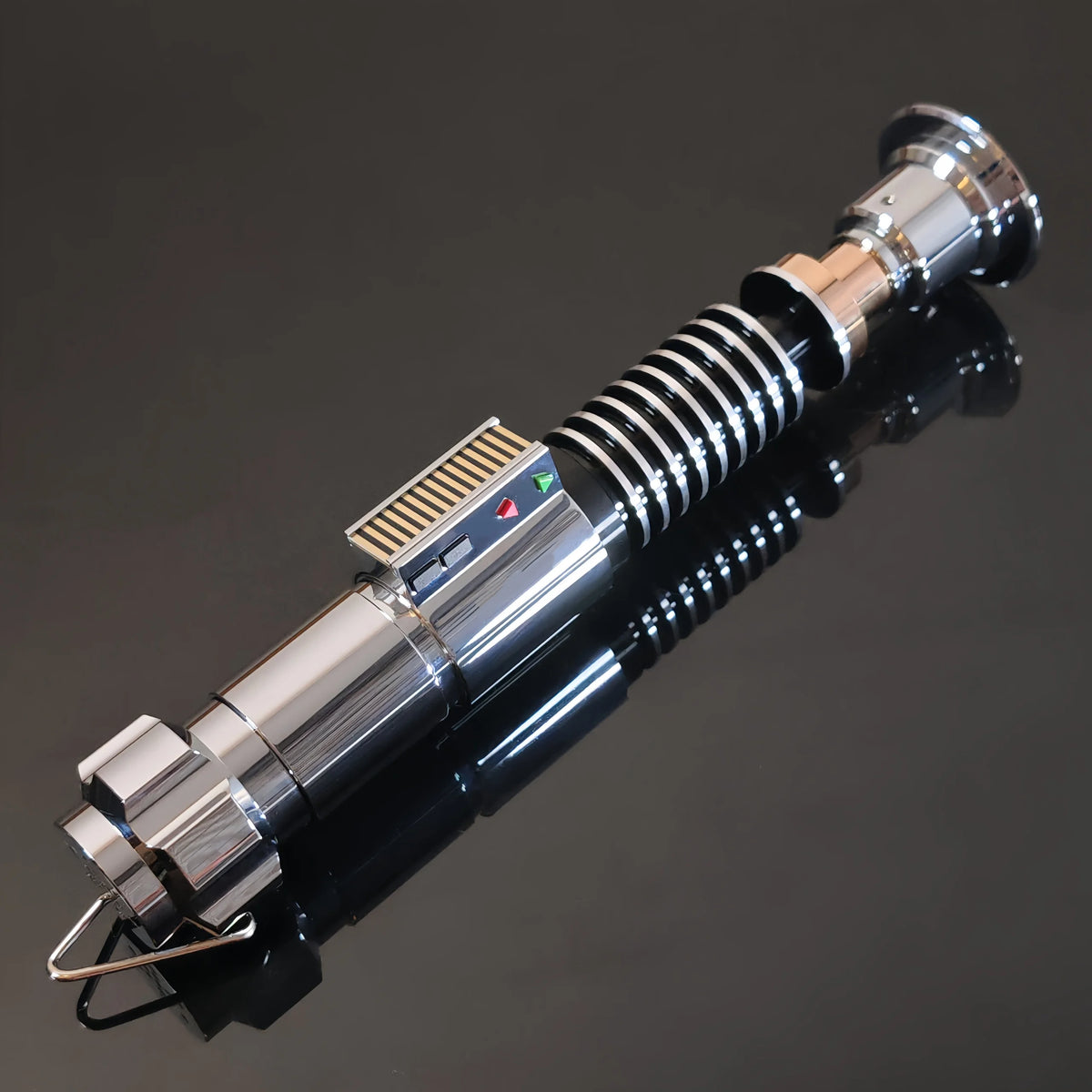 A metallic lightsaber hilt with a Bluetooth motion sensor and blade tip, displayed on a dark reflective surface.