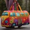 A vibrant orange and purple quilted travel duffle bag with green accents is being carried by a person outdoors.