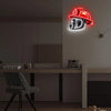 A red firefighter helmet neon sign with a silver letter D is mounted on a wall above a modern desk.