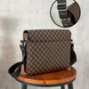 A brown patterned leather crossbody bag with a black strap resting on a wooden stool.