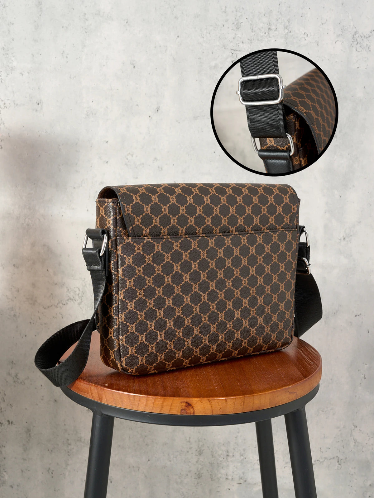 A brown patterned leather crossbody bag with a black strap resting on a wooden stool.