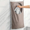 A hand is pulling out a folded gray towel from a fabric laundry storage bag hanging on a white marble tile wall.