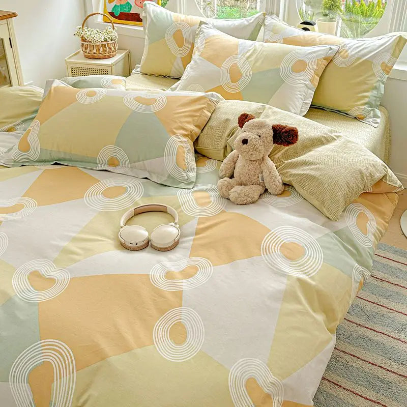 A set of yellow and white patterned cotton duvet cover and pillow shams with a stuffed animal on the bed.