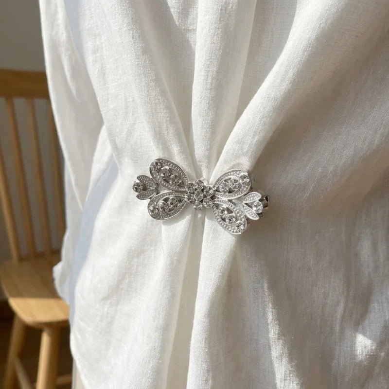 Silver rhinestone bowknot clothing clips securing a white fabric garment