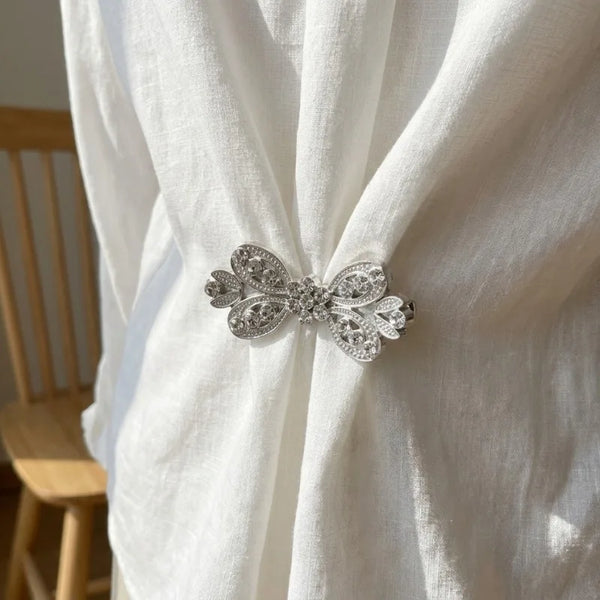 Silver rhinestone bowknot clothing clips securing a white fabric garment