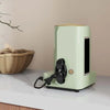 A light green cord organizer and wire winder device sits on a white surface next to a woven basket.