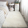 A fluffy white silk-touch area rug placed on a light wooden floor next to a bedside table.