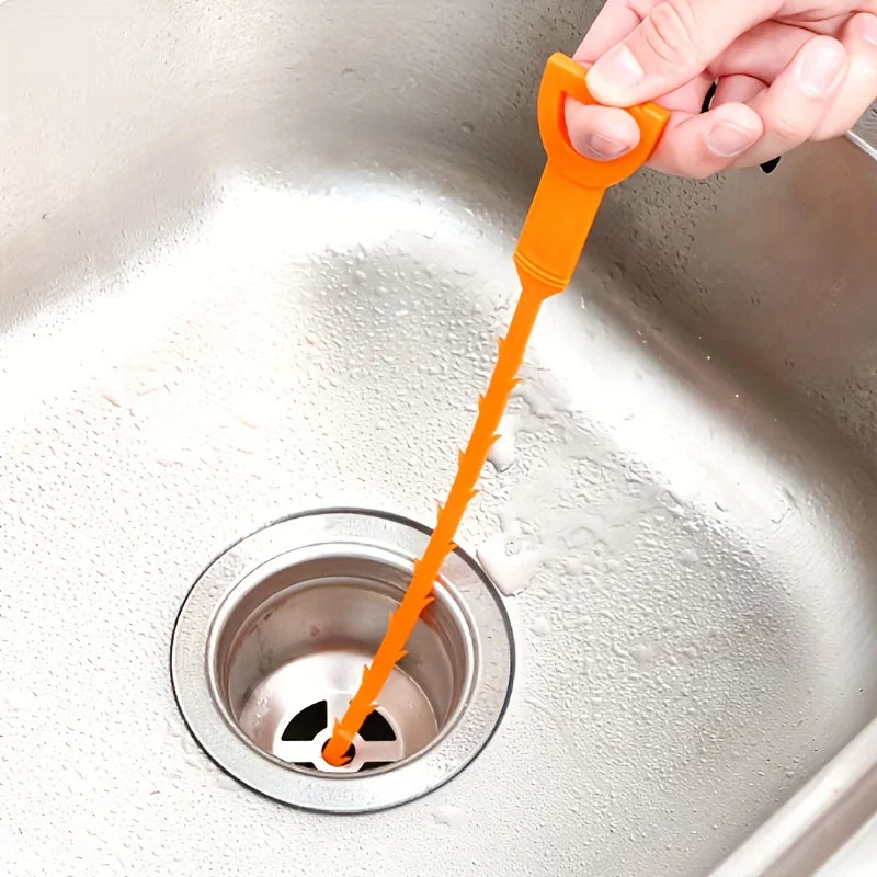 A hand is using an orange flexible drain cleaning tool to clear a sink drain.