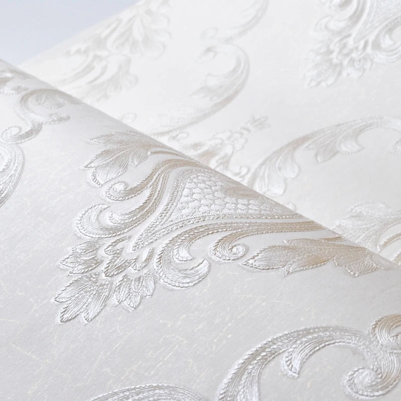 Close-up of an embossed damask wallpaper roll featuring a delicate floral design in white.