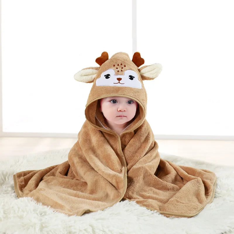 A baby wearing a brown fuzzy hooded towel with a cartoon animal design lying on a white surface.