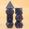 A set of five black polyhedral dice with purple accents arranged vertically on a light background.