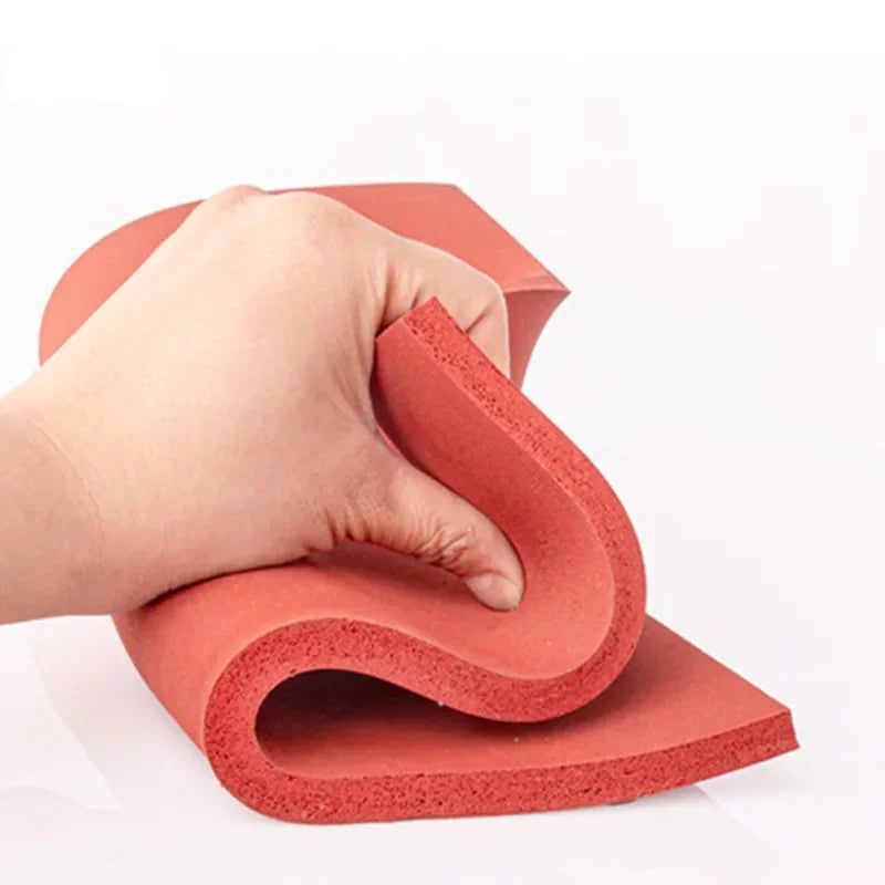 A hand is bending a red silicone heat-resistant craft mat into a curved shape.