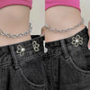A close-up of a person wearing black jeans with silver chains and flower waist clips, paired with a pink top.