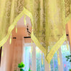 A sheer lime green lace curtain valance with gold trim hangs over a window.