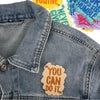 A denim jacket featuring colorful embroidered iron-on patches with positive and humorous sayings