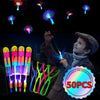 A boy is launching glowing LED flying arrow toys into the air against a dark background.