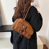 Eine Frau hält eine braune Handtasche mit mehreren Fächern vor einem weißen Hintergrund.