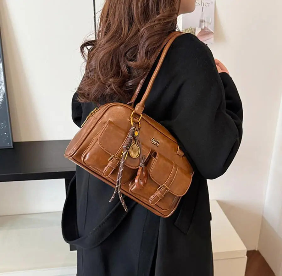 Eine Frau hält eine braune Handtasche mit mehreren Fächern vor einem weißen Hintergrund.