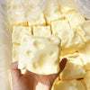 A hand holds a block of realistic cheese squishy stress relief fidget toy inside a clear plastic bag.