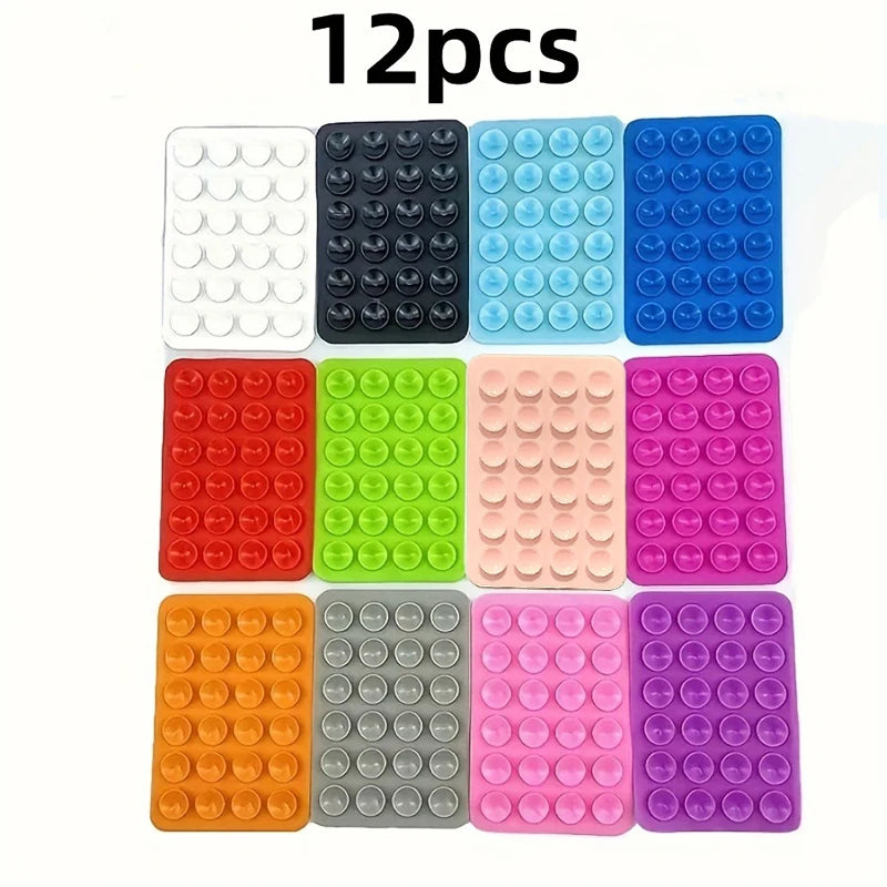 A set of 12 reusable silicone suction phone mounts in various colors including white, black, light blue, and pink.
