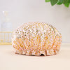 A pink and gold leopard print reusable elastic shower cap resting on a light surface.