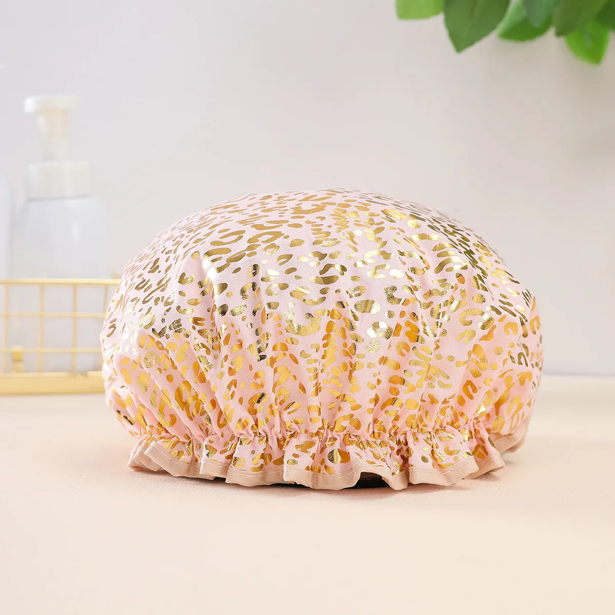A pink and gold leopard print reusable elastic shower cap resting on a light surface.