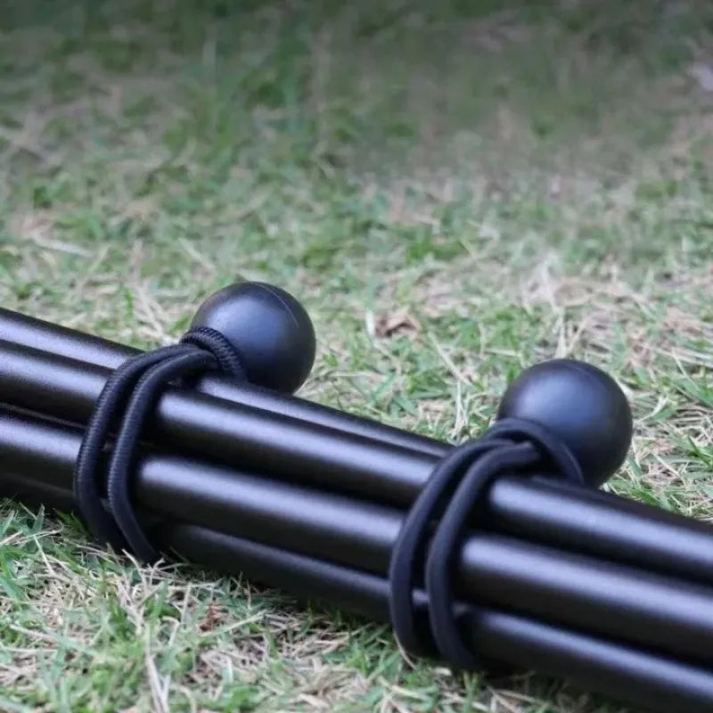 Black elastic tent tie-down ropes with plastic buckles lying on green grass