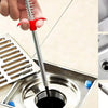 A hand is using a flexible drain snake with a red handle to clear a clog in a kitchen sink.