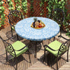 A round table set outdoors featuring a blue and white patterned tablecloth, a wooden deck, and black wrought iron chairs.