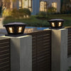 Outdoor solar post cap lights with warm LED illuminating a wooden fence and patio area.