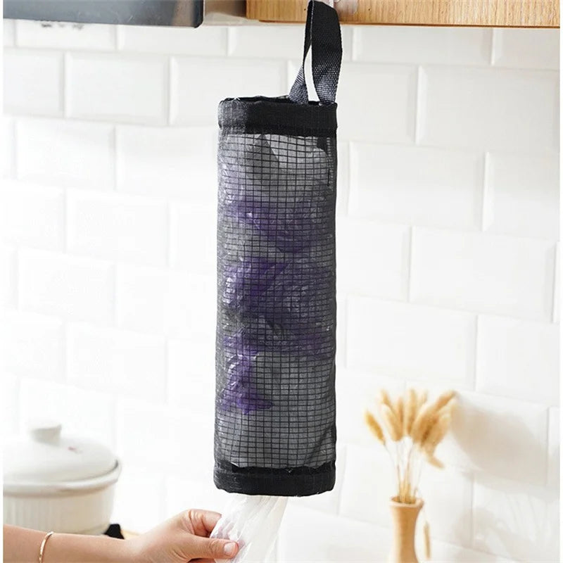 A black mesh bag dispenser hanging on a kitchen shelf, with a hand holding the bottom of the bag.