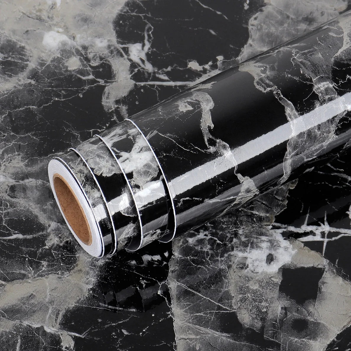 A roll of waterproof self-adhesive marble wallpaper, silver and white marbled pattern, lying on a dark marble surface.