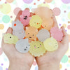 A hand holds a collection of pink and yellow kawaii animal squishies toys against a colorful, bokeh background.