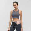 A woman models a gray sports bra and dark pants with a beige nylon waist pack.