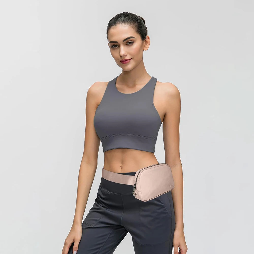 A woman models a gray sports bra and dark pants with a beige nylon waist pack.