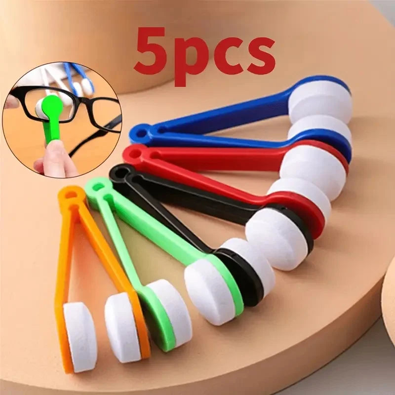 A set of five eyeglass cleaning tools including brushes and microfiber cloths displayed on a light brown surface.