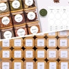 A collection of square glass spice jars with bamboo lids and labels featuring various spices like Mung Bean, Star Anise, Red 