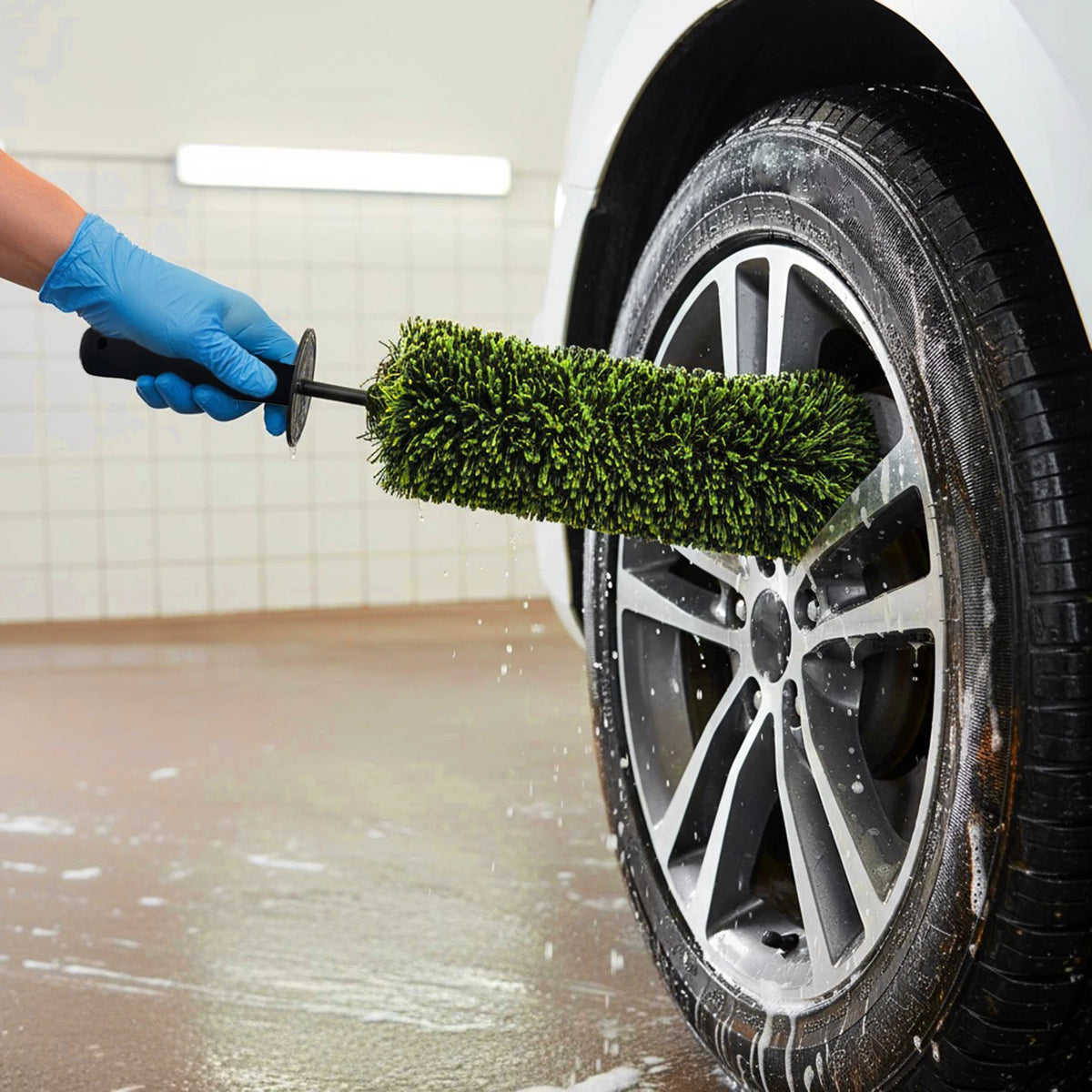 A hand is using a green wheel barrel brush with an ergonomic handle to clean the rim of a car tire.