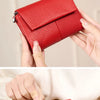 A red leather tri-fold wallet with a zipper and coin pocket being held by hands.