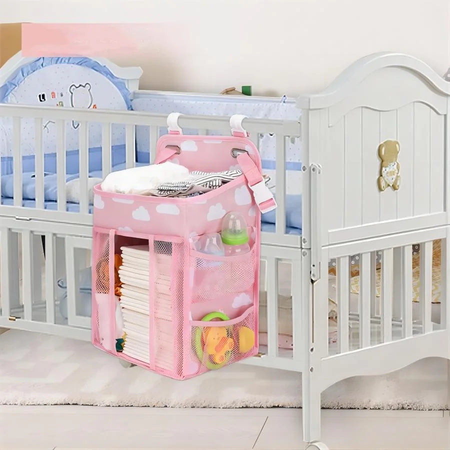 A pink hanging diaper storage organizer with multiple compartments is shown inside a white crib.
