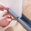 Hands are using pliers to install a draft blocker under a door seal on a wooden floor.