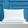 A white rectangular pillow resting on a light gray surface against a blue paneled background.