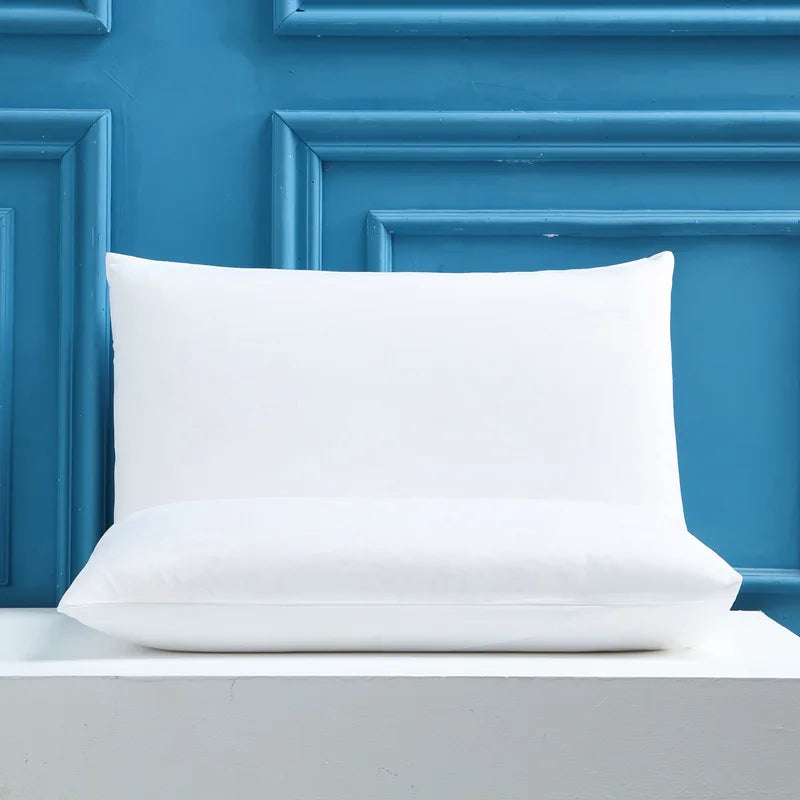 A white rectangular pillow resting on a light gray surface against a blue paneled background.